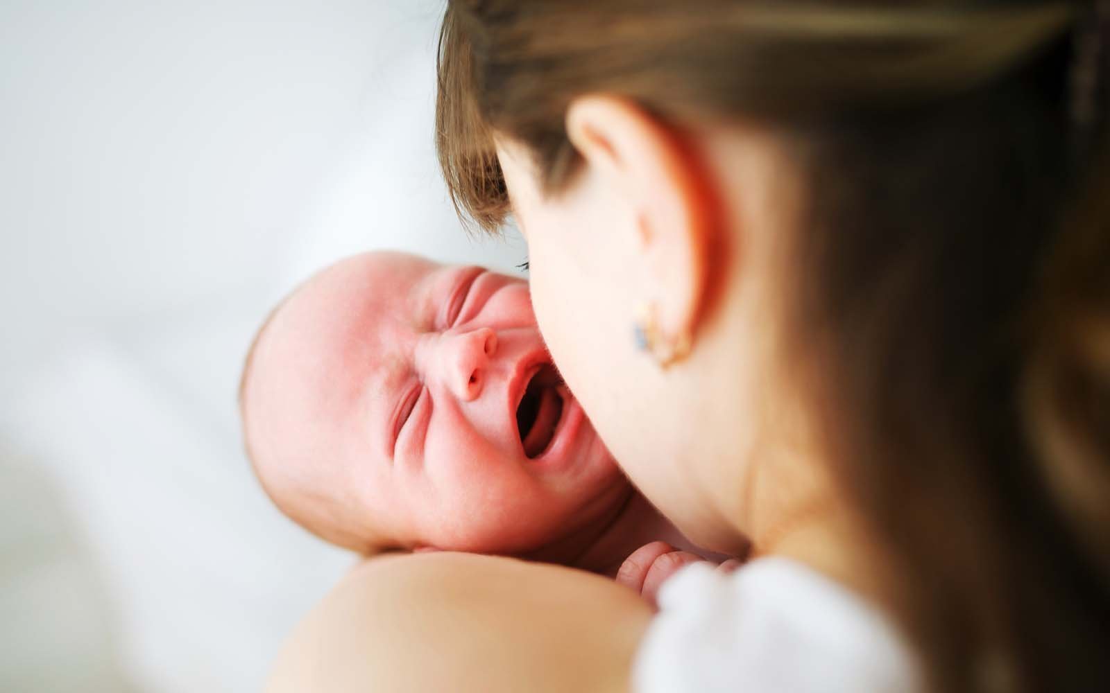 Newborn baby crying in mother's arms, overtired