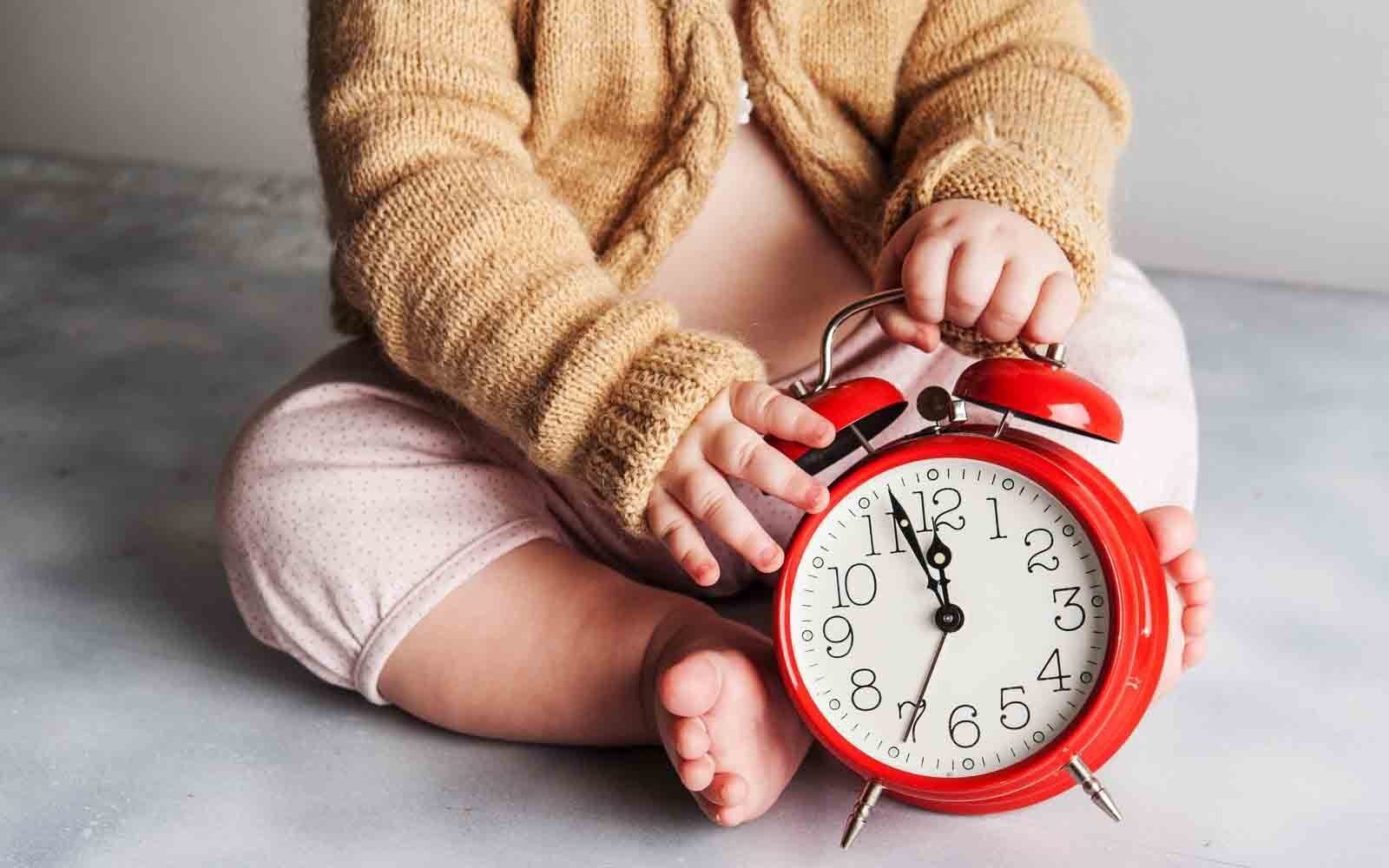 Baby holding a clock showing that they are waking every two hours